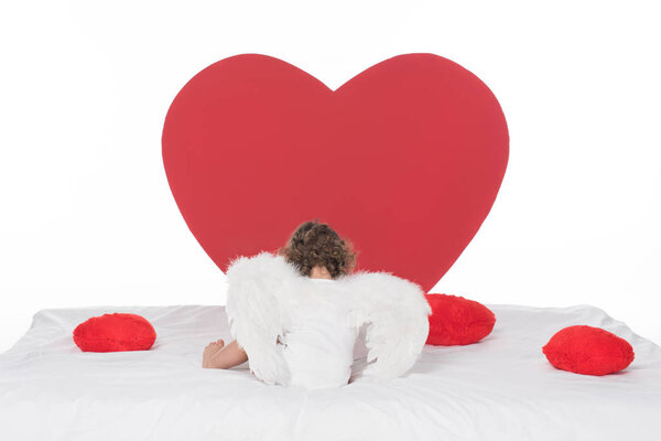 little cherub with wings lying on bed with hearts, isolated on white