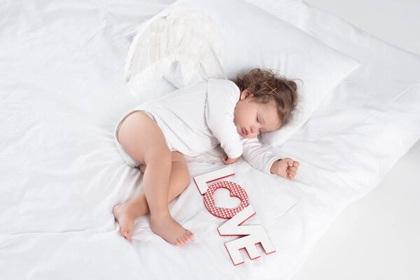 little cherub with wings lying on bed with love sign