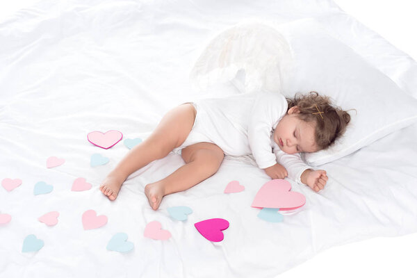 little sleepy cherub with wings lying on bed with hearts 