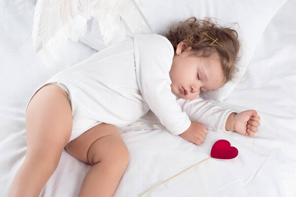 cute cherub with wings lying on bed with heart 