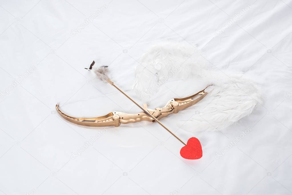top view of wings, bow and arrow on white bed