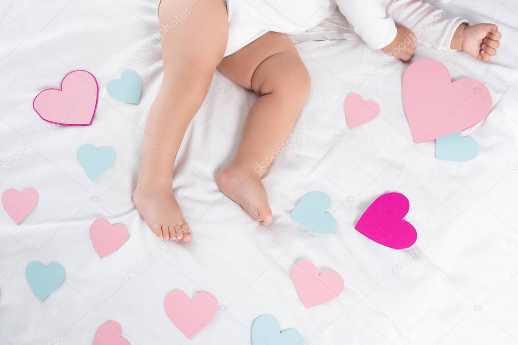 cropped view of little baby lying on bed with hearts 