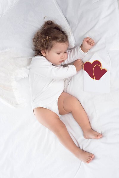 little cherub with wings lying on bed with hearts 
