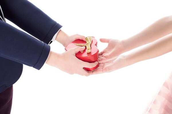 cropped shot of boy in suit presenting heart shaped gift box to little girl isolated on white