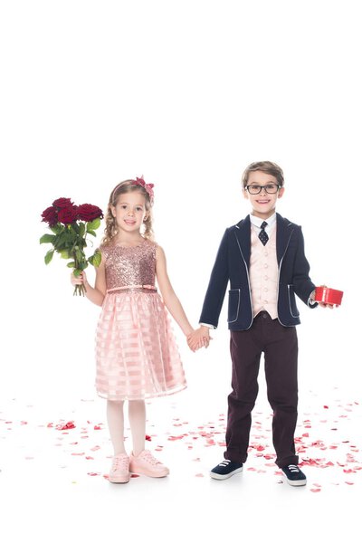 adorable happy kids with roses and heart shaped gift box holding hands and smiling at camera on white    