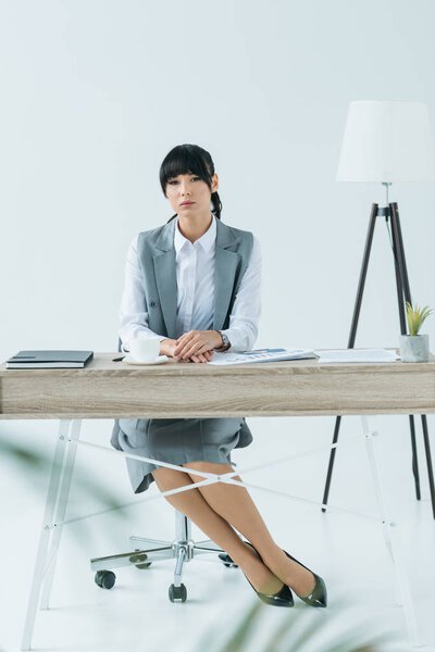 beautiful businesswoman sitting at table and looking at camera on gray