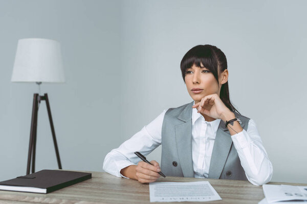 thoughtful businesswoman signing contract isolated on gray