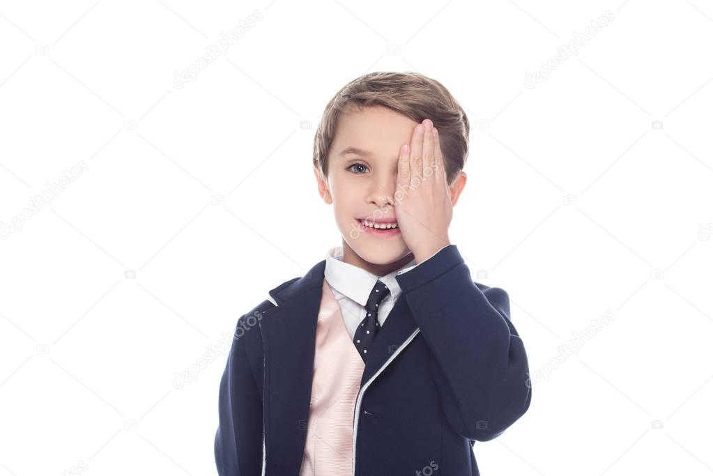cute little boy closing eye with palm and smiling at camera isolated on white
