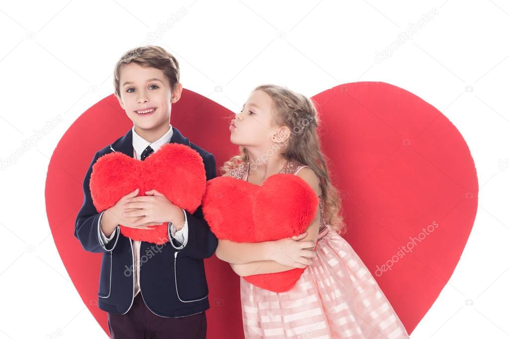 cute little kids holding heart shaped pillows and able to kiss isolated on white 