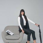 Attraktive brünette Geschäftsfrau sitzt auf Sessel mit Regenschirm isoliert auf grau