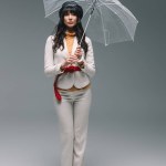 Morena mujer en traje blanco de pie con paraguas en gris