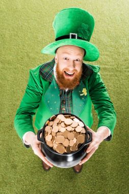 excited leprechaun holding pot of gold on green grass clipart