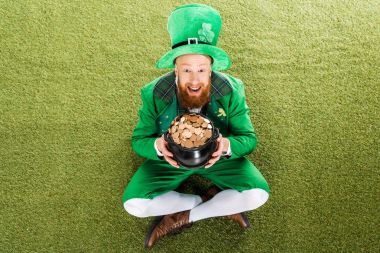 excited leprechaun with pot of gold sitting on green grass clipart