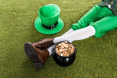 cropped view of leprechaun with hat and pot of gold sitting on green grass clipart