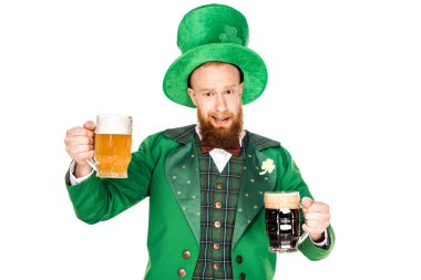 handsome bearded man in green costume and hat holding glasses of beer and looking at camera isolated on white  