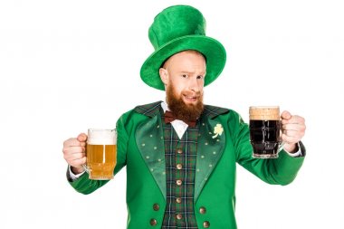 bearded man in green costume and hat holding glasses of beer and looking at camera isolated on white 