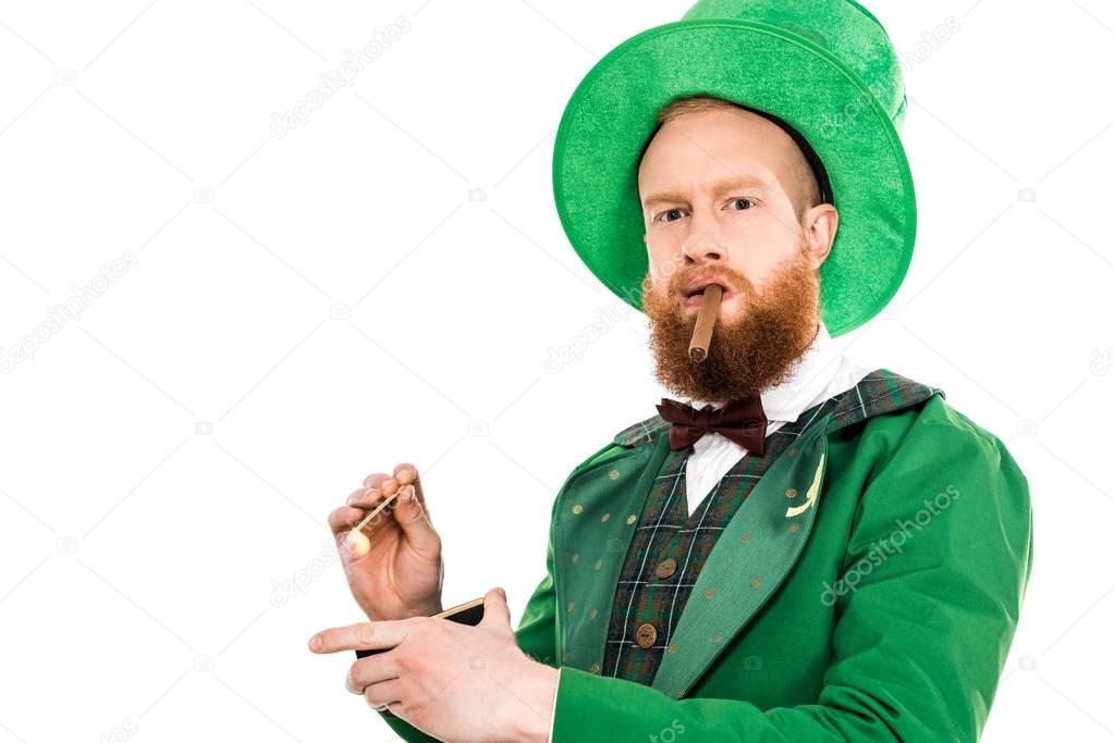 leprechaun in green costume and hat smoking cigar and looking at camera isolated on white