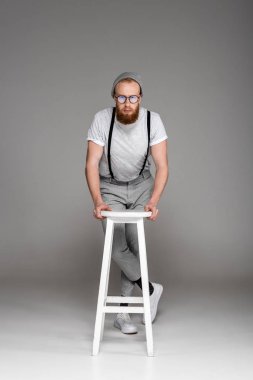şık sakallı adam Stool'da yaslanmış ve gri kameraya bakarak eyeglasees içinde 