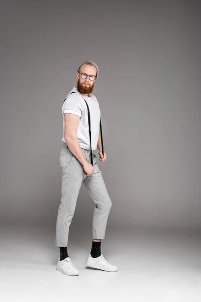 Fashionable Bearded Man Spectacles Holding Suspenders Looking Camera Grey — Stock Photo, Image