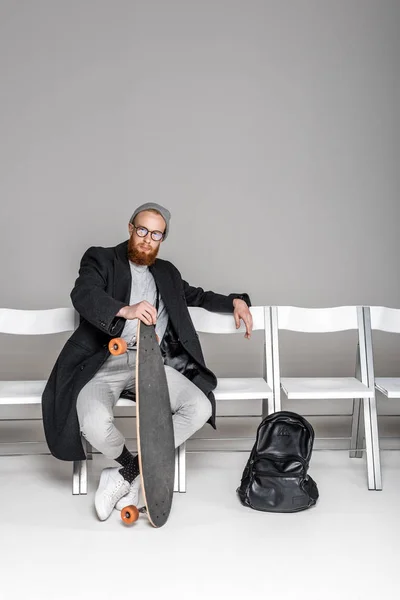 Stylish Man Overcoat Spectacles Holding Skateboard While Sitting Chair Grey — Free Stock Photo