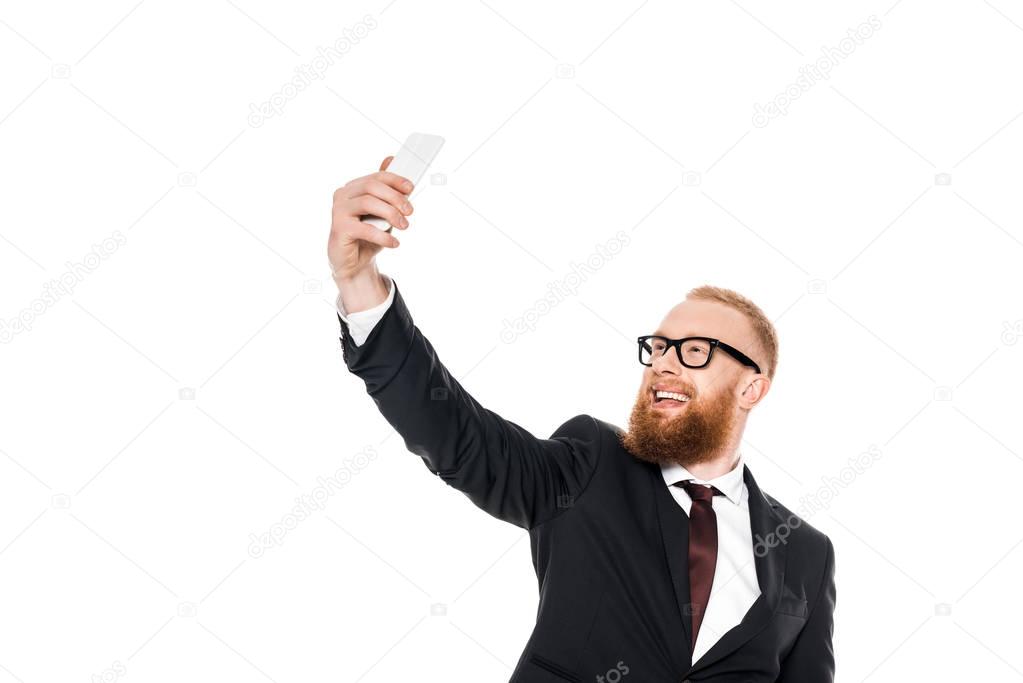 cheerful young businessman in eyeglasses taking selfie with smartphone isolated on white 