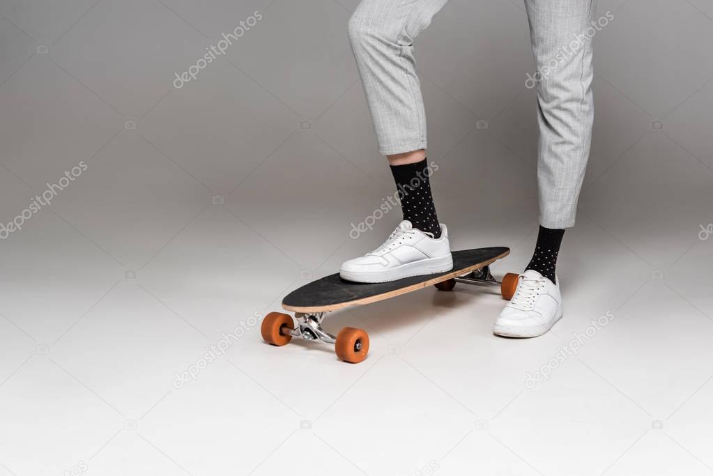 low section of stylish man standing on skateboard on grey