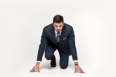 serious young businessman in starting position ready to run isolated on grey clipart