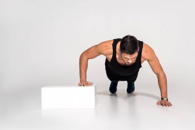 handsome young man doing push ups with one hand on block