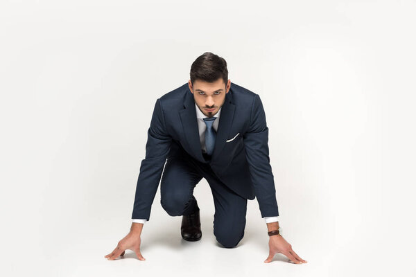 serious young businessman in starting position ready to run isolated on grey