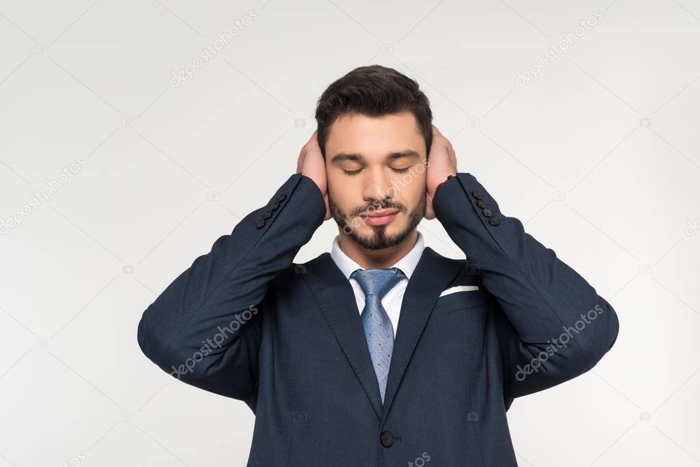 relaxed young businessman with closed eyes closing ears with hands isolated on grey