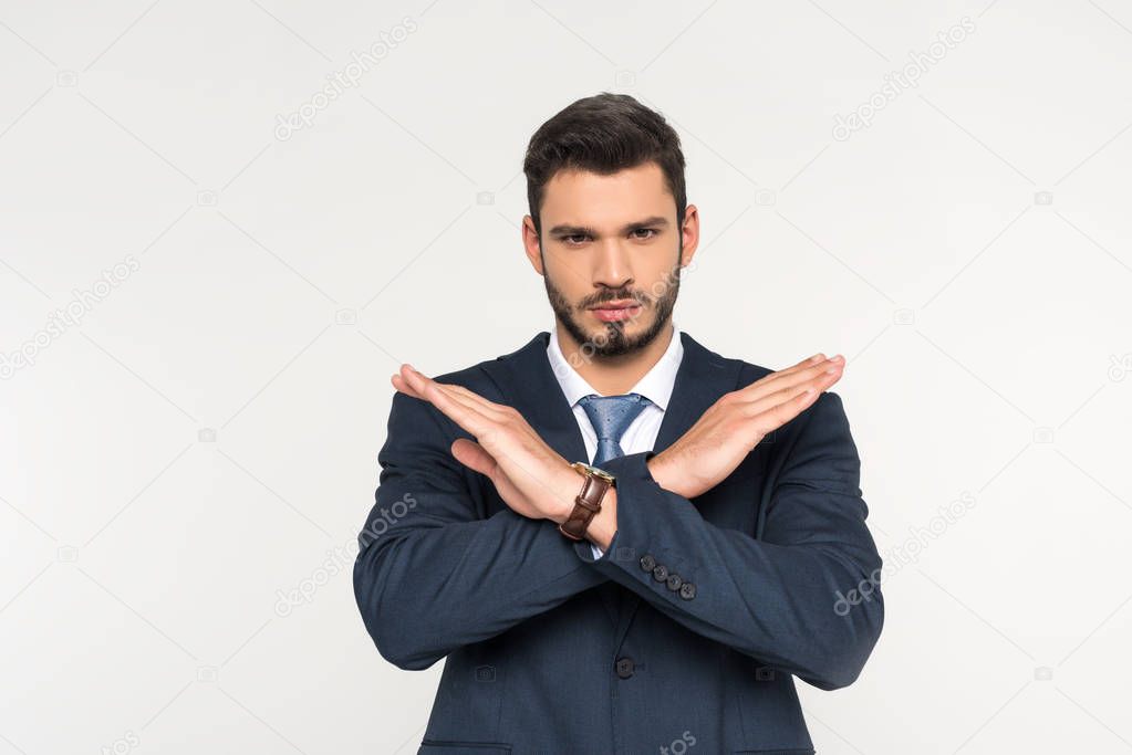 serious young businessman crossing hands and looking at camera isolated on grey