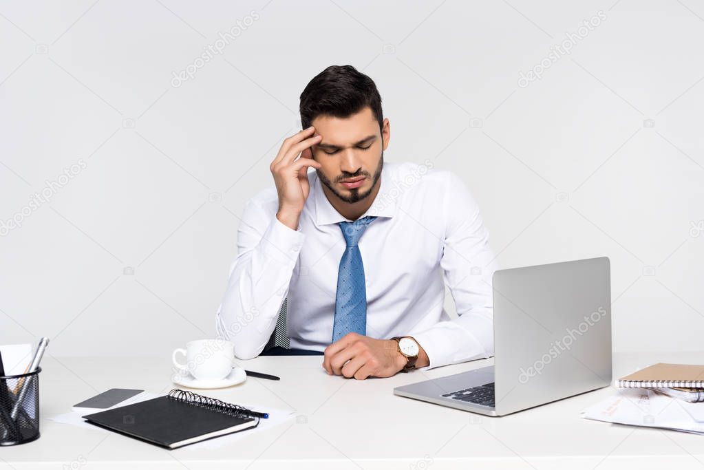 overworked young businessman suffering from headache while sitting at workplace 