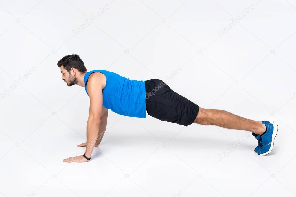 side view of young man doing push ups on white