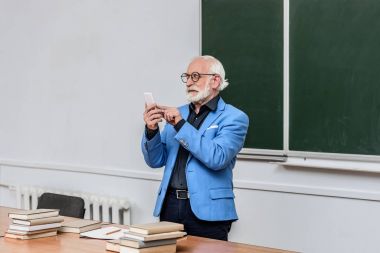 gri saç Profesör smartphone konferans odasında bakarak