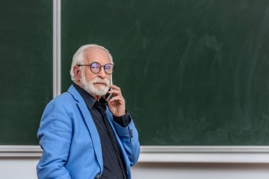 gri saç Profesör Smartphone ile konuşmak ve kameraya bakıyor