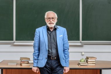 Konferans odasında duran ve kameraya bakarak gülümseyen gri saç Profesör