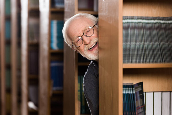 happy grey hair librarian looking out from shelf 