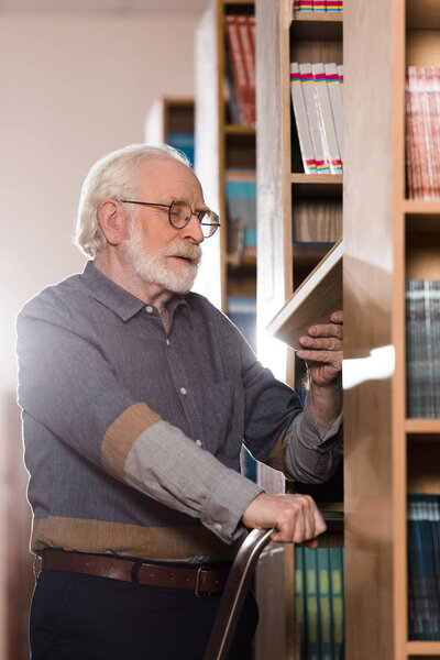 grey hair librarian looking at book in hand