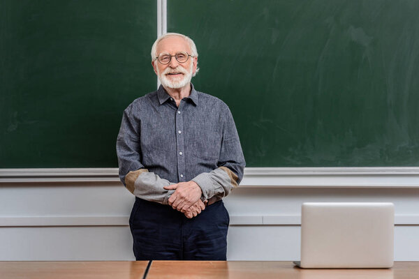 smiling senior lecturer standing in classroom and looking at camera