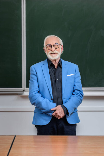 smiling senior lecturer standing in classroom and looking at camera
