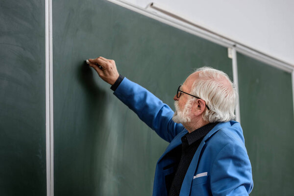 side view of senior lecturer writing something on blackboard with piece of chalk