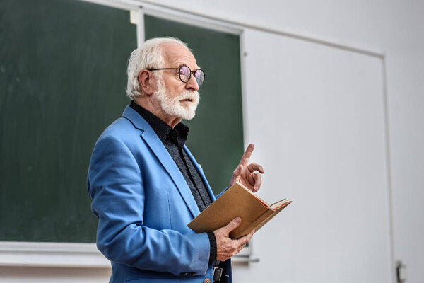 senior lecturer holding book and showing one finger up