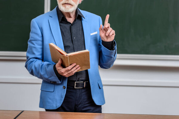 cropped image of senior lecturer holding book and showing one finger up