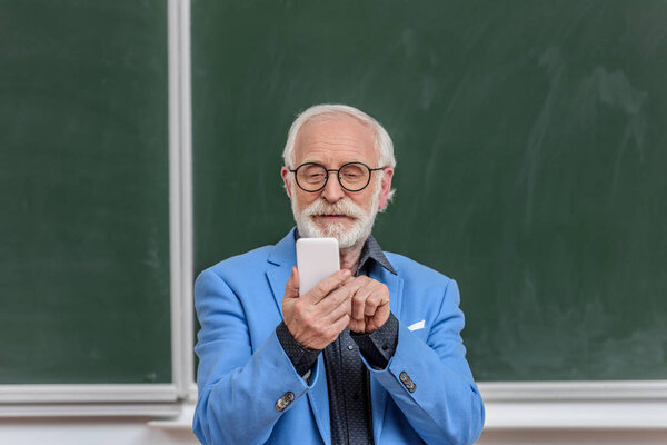 smiling grey hair professor looking at smartphone in lecture room
