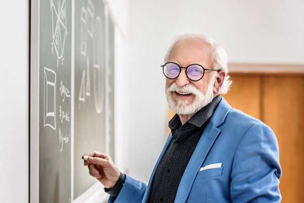 smiling grey hair professor holding piece of chalk