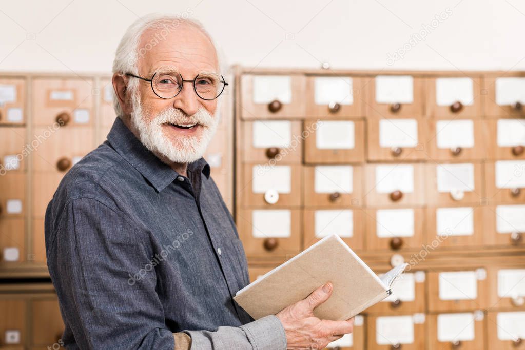smiling senior male archivist holding book and looking at camera