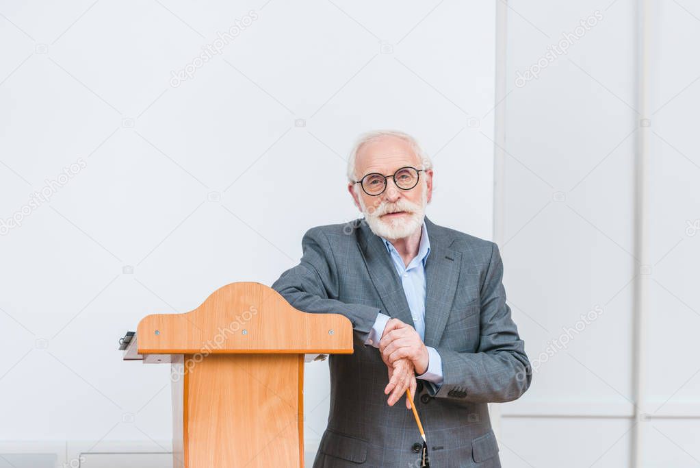 senior lecturer leaning on wooden tribune in classroom