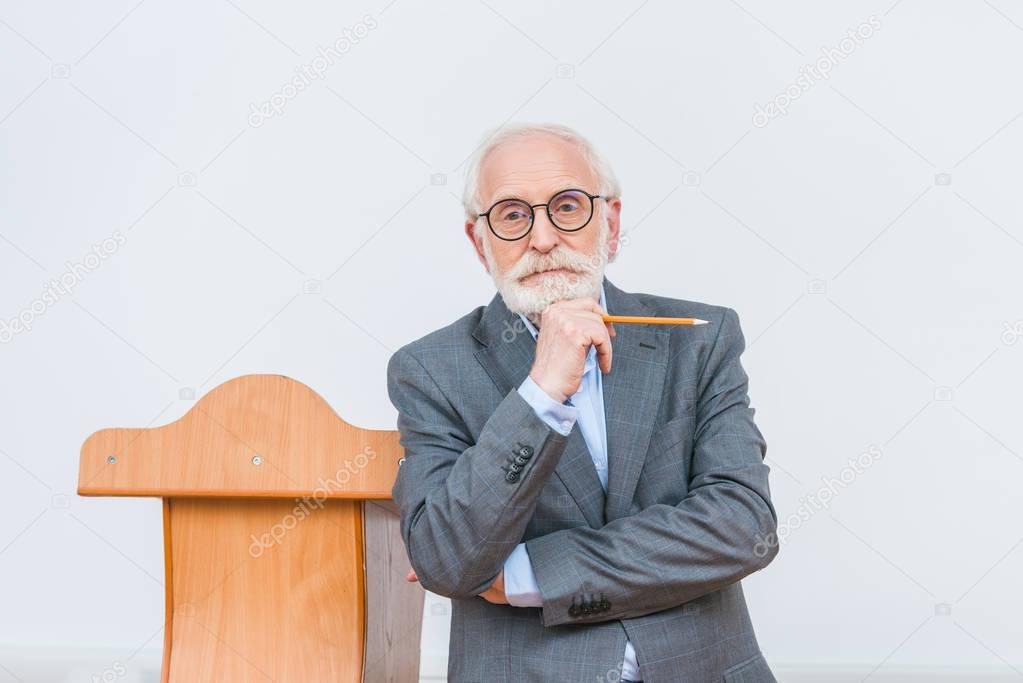 pensive senior lecturer standing with pencil isolated on white