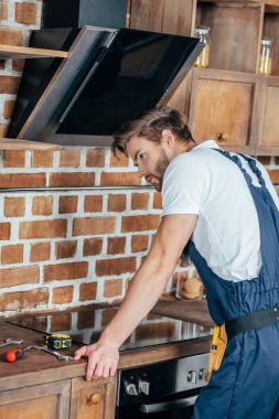 Genç tamirci mutfakta fırın, eğilerek koruyucu iş giysisi