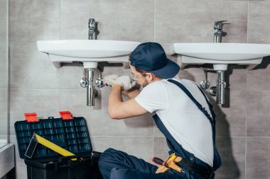 back view of young professional plumber fixing sink in bathroom clipart